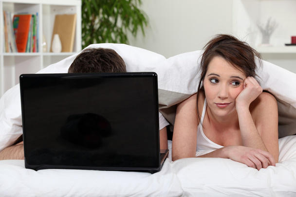 Unimpressed woman in bed with her partner and his laptop - Photo, image