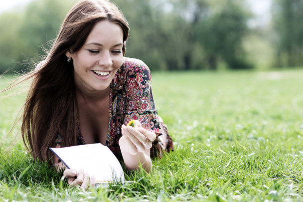 Young beautiful woman lays on a grass in park with a diary in ha - Fotografie, Obrázek