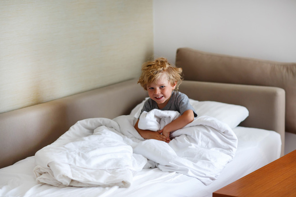 entzückendes Kind Junge nach dem Schlafen in seinem weißen Bett mit Spielzeug - Foto, Bild