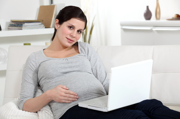 Pregnant woman resting laptop on lap - 写真・画像