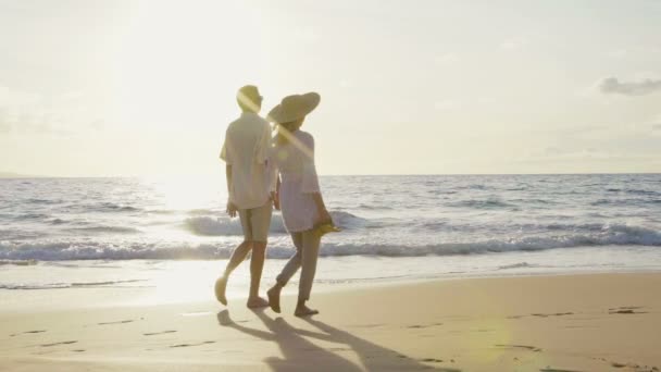 Sonnenuntergangsspaziergang in Zeitlupe an einem Luxusstrand. Älteres Paar hält Händchen und geht bei Sonnenuntergang den Strand hinunter und bekommt nasse Füße - Filmmaterial, Video