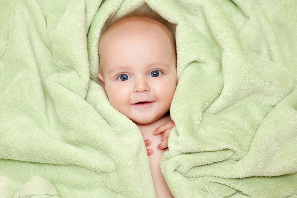 Caucasian baby boy covered with green towel joyfully smiles - 写真・画像