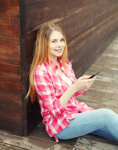 Menina sorrindo jovem usando smartphone sentado na cidade
 - Foto, Imagem