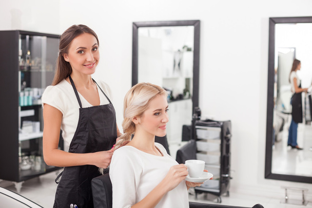 Beautiful blond girl is getting hairstyle by hairdresser - Fotó, kép