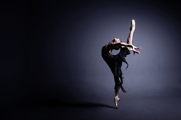 Young ballerina in dark cloth is dancing in a dark of the photostudio - Photo, image