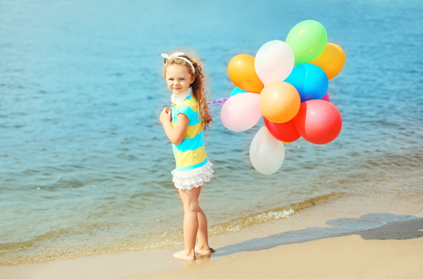 Onnellinen lapsi kesärannalla värikkäillä ilmapalloilla lähellä merta
 - Valokuva, kuva
