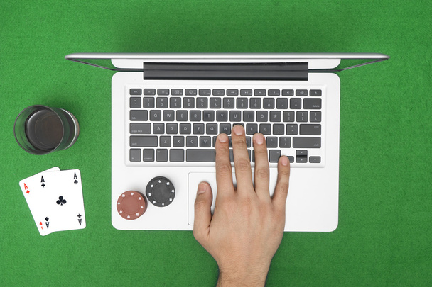 Man playing online poker with laptop on a green table with chips - Foto, afbeelding