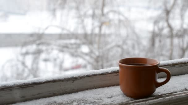 Csésze kávé a régi ablakpárkányon, háttérben a hóesésben - Felvétel, videó