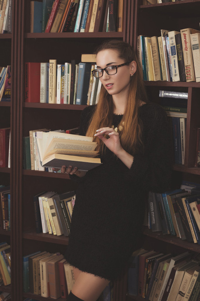 nuori kaunis tyttö musta mekko seisoo kirjastossa kirjoja
 - Valokuva, kuva