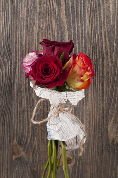 Bunch of multicolor rose flowers wrapped in newspaper over woode - Foto, imagen