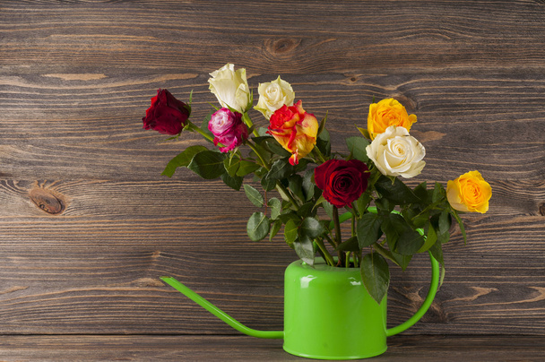 Bouquet of multicolor roses in watering can over wooden backgrou - Foto, Imagem