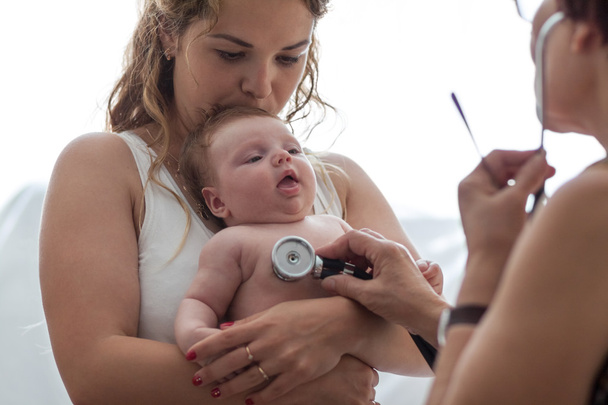 Lääkäri tutkii vastasyntyneen tytön stetoskoopilla
 - Valokuva, kuva