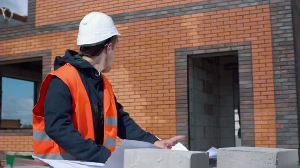Architect looking at blueprints in a building site - Кадры, видео