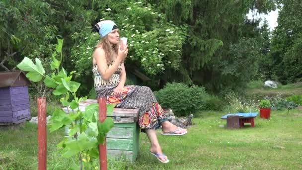mulher louca no vestido beber cocktail de frutas saudável sentado na colmeia de abelhas. 4K
 - Filmagem, Vídeo