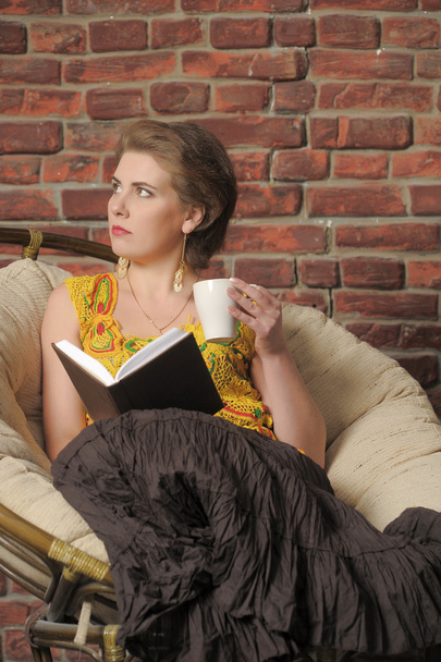 Woman with a book and a cup in the chair. - Photo, Image