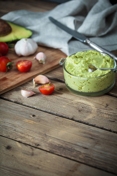 Guacamole on wooden table surrounded by its ingredient - Foto, Bild
