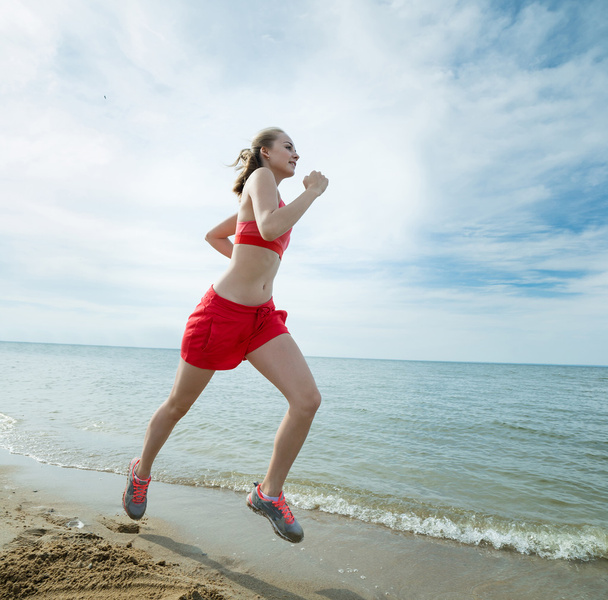 Young lady running at the sunny summer sand beach. Workout.  Jog - Zdjęcie, obraz