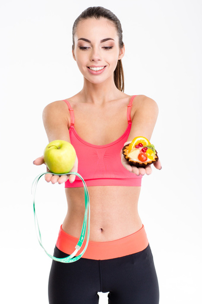 Joyful cute fitness woman making decision between apple and cake  - Fotografie, Obrázek