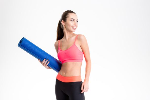Cheerful beautiful fitness woman holding yoga mat and looking away - Photo, Image