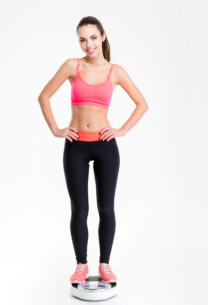 Attactive smiling young fitness woman standing on weighing scale - Foto, afbeelding