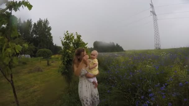madre con el bebé en brazos va en el prado bajo la lluvia de verano. 4K
 - Metraje, vídeo