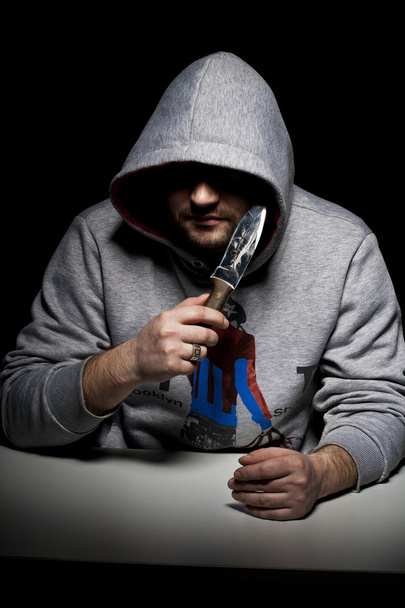 Man at table in hood with knife - Фото, зображення