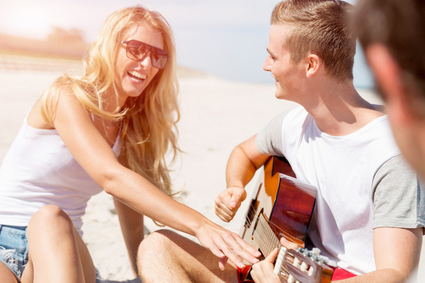 Beautiful young people with guitar on beach - Фото, изображение