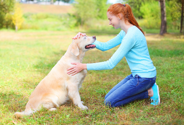 Happy owner woman stroking Golden Retriever dog on grass in park - Photo, image