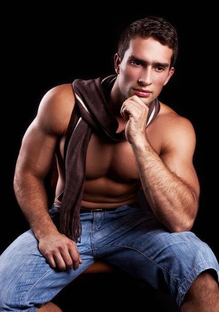 Young muscular man sitting on a chair and thinking, isolated on black - Foto, imagen