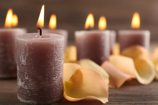 Светлая восковая свеча с лепестками цветов на деревянном фоне
 - Фото, изображение