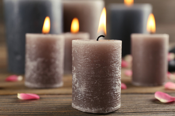 Alight wax grey candle with flower petals and pebbles on wooden background - Foto, Bild