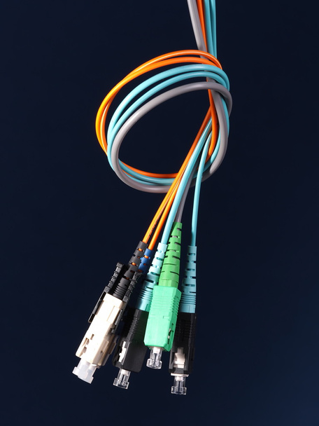 Um pacote de três cabos de fibra óptica com conectores dispostos em um nó sobre fundo preto
 - Foto, Imagem