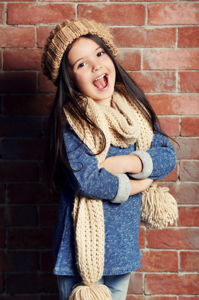 Portrait of little fashion kid girl in knitted cap and scarf on bricks wall background - Foto, Bild