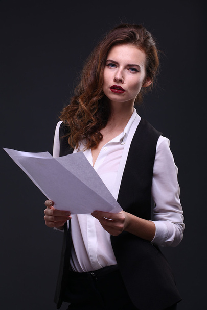 Beautiful business lady holding white sheet of paper on a dark background. Studio shot - 写真・画像