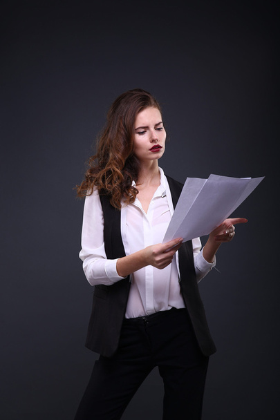 Beautiful business lady holding white sheet of paper on a dark background. Studio shot - Foto, Imagem