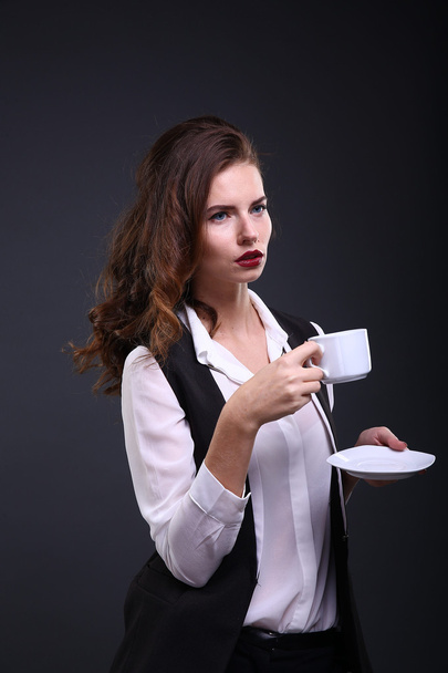Красивая деловая леди держит белую чашку кофе на темном фоне. Снимок студии
 - Фото, изображение