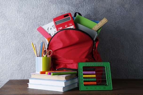 Backpack with school supplies on wooden table, on grey wall background - 写真・画像