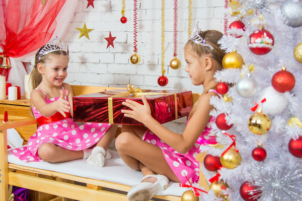 Tyttö antaa iso punainen joululahja toinen tyttö istuu penkillä
 - Valokuva, kuva
