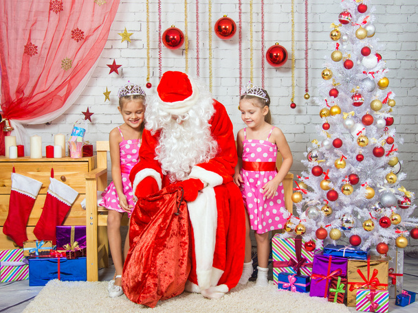 Santa Claus pulls out a bag of gifts to two girls - Fotografie, Obrázek