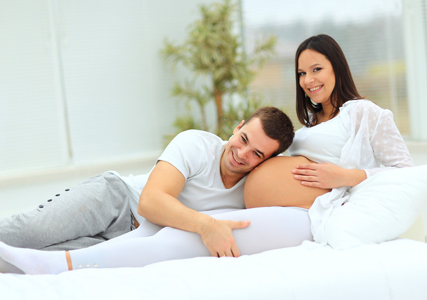 the man leaned against  to the baby bump of his pregnant wife, who is lying on the bed - Foto, Imagen