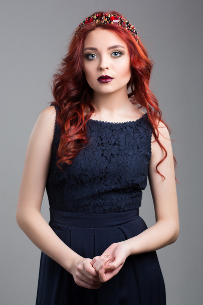 Beautiful red-haired fashion model posing in evening dress and in the diadem over dark background. - Fotó, kép