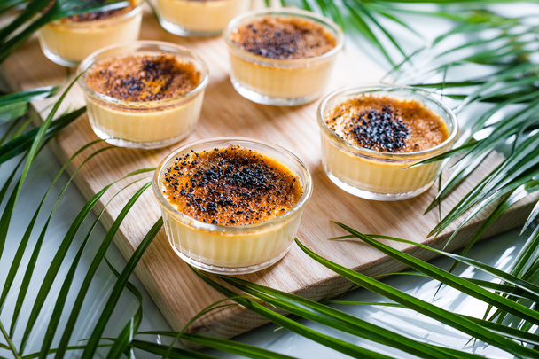 Creme brulee op houten dienblad, gedecoreerd met palmbladeren. Traditionele Franse vanille crème dessert met gekaramelliseerde suiker op bovenkant. - Foto, afbeelding