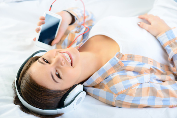 Positive girl lying in bed and listening to music. - Photo, Image