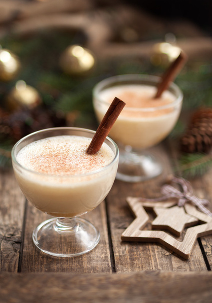 Eggnog christmas homemade winter egg, milk, rum, vanilla alcohol liqueur preparation recipe in two cups with cinnamon sticks on wooden vintage table. shallow depth of field. - Photo, Image