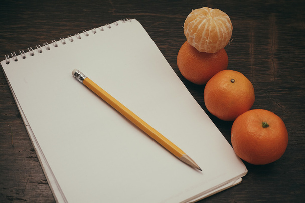 Tangerines notebook pencil coffee on old wooden background - Фото, изображение