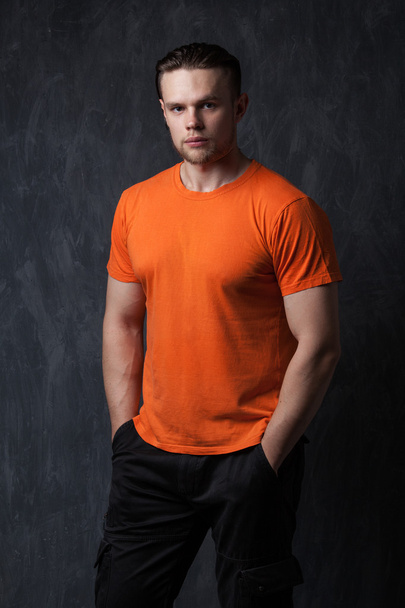 Strong man in an orange shirt tucked hands in his pockets - Foto, Imagen