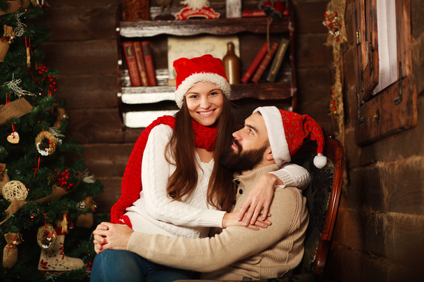 Cheerful couple in Christmas hats having fun in a country house - Foto, Imagen