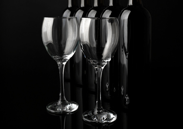 Glasses and wine bottles in a row on black  background, close up - Photo, image