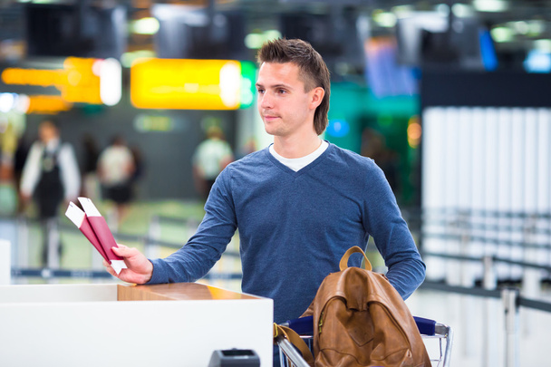 Молодой человек с паспортами и посадочными талонами на стойке регистрации в аэропорту
 - Фото, изображение