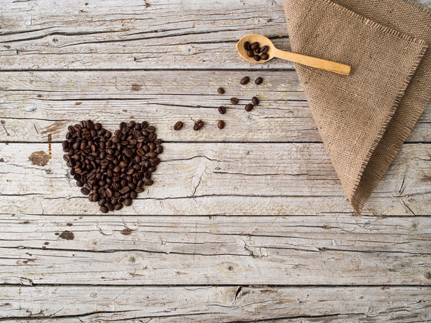 Heart shape made of coffee beans and wooden spoon on wooden back - Фото, зображення